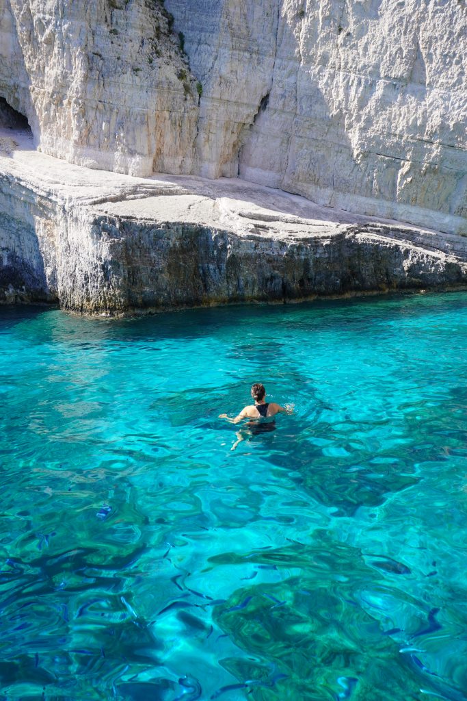 Guest swimming in crystal clear turquoise waters near white cliffs in Zakynthos